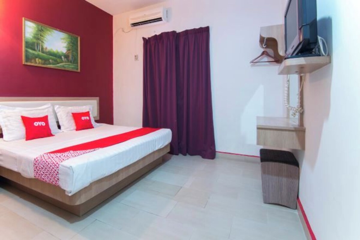A hotel room with a bed, a TV, a painting on the wall, and a window with curtains.