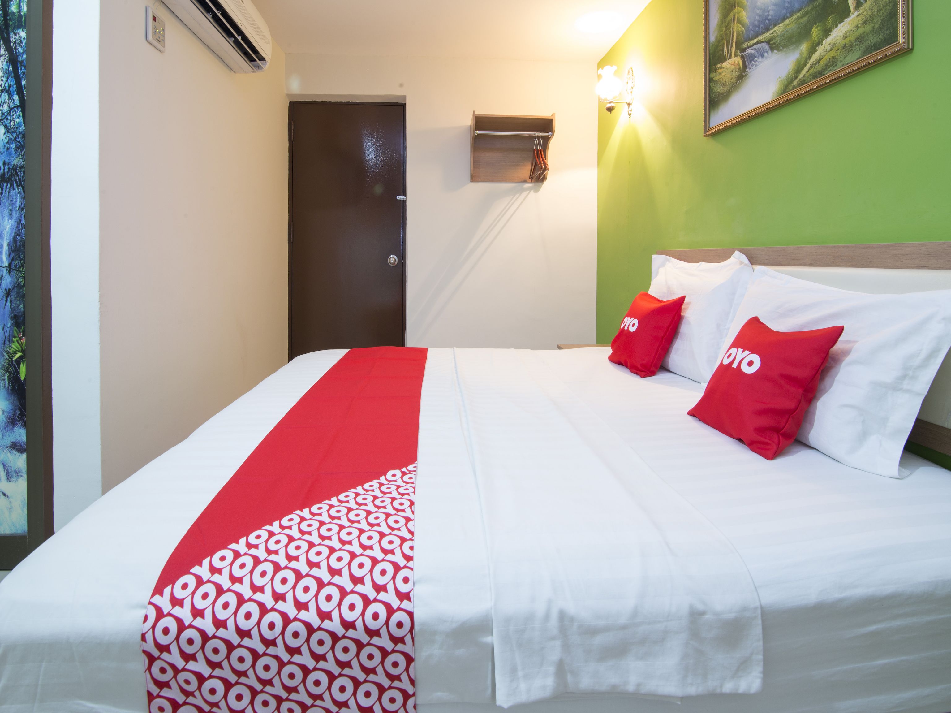 Ein Hotelzimmer mit einem Bett, einer roten und weißen Bettdecke, zwei roten Kissen, einer grünen Wand und einem Bild eines Wasserfalls.