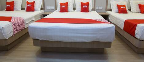 Habitación de hotel con tres camas, cada una con ropa de cama blanca y almohadas rojas, y una manta de colores rojo y blanco.