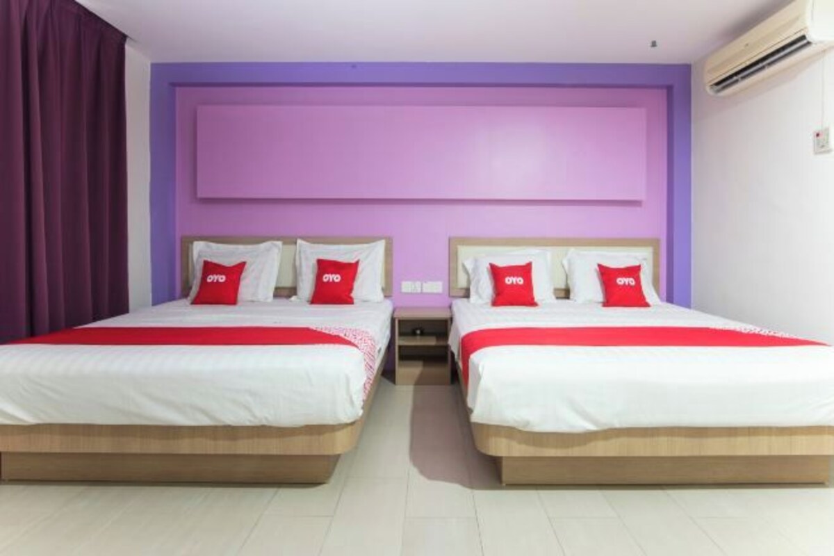 A hotel room with two beds, each with red and white bedding, and a purple accent wall.