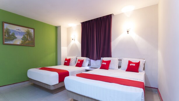 A hotel room with two beds, each with white bedding and red accents, a green wall, and a painting of a landscape. - Valley View Hotel (Lumut)