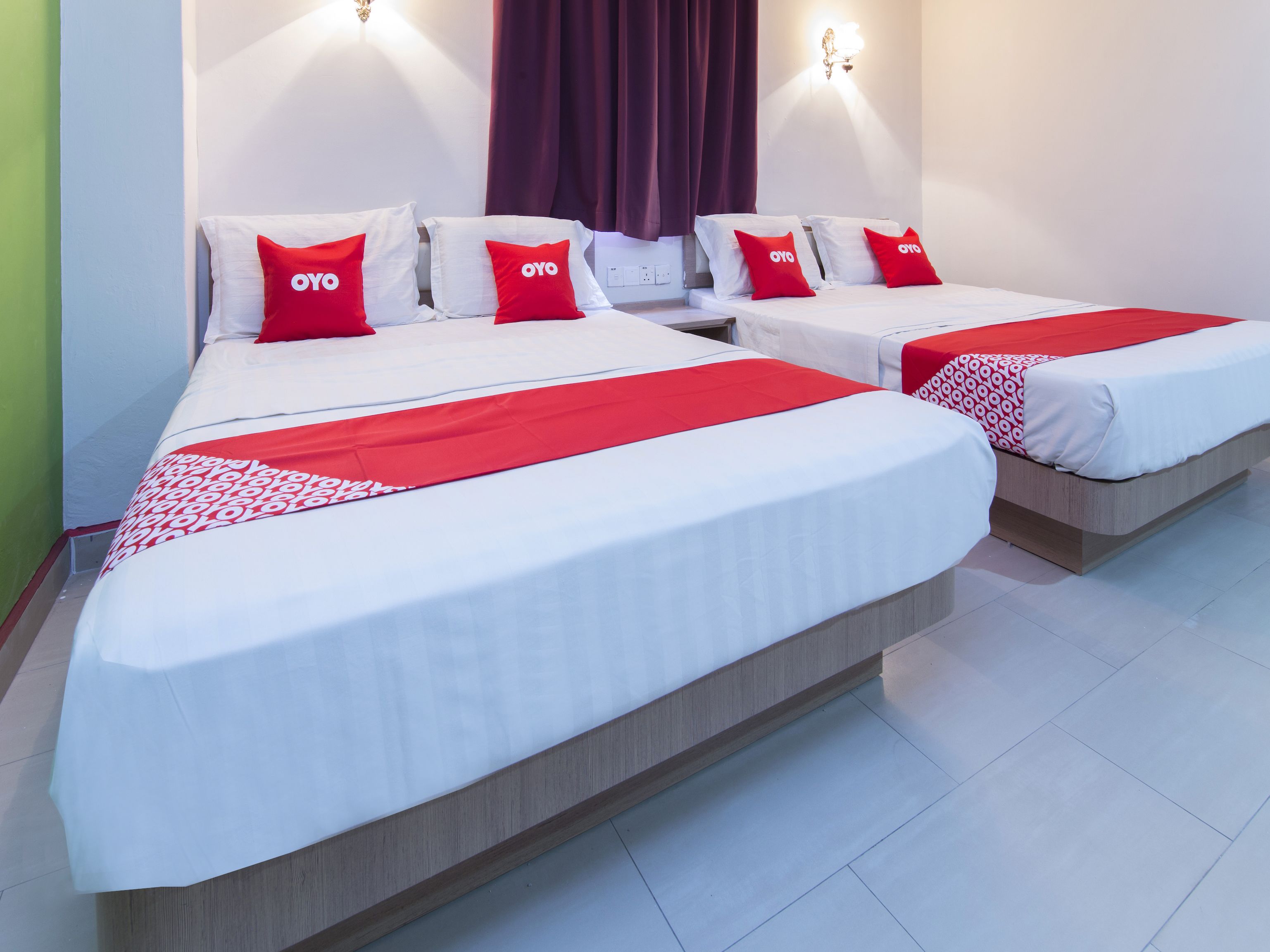 A hotel room with two beds, each with white bedding and red accents, including pillows and a blanket.