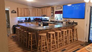 A kitchen with wooden cabinets, a central island with stools, a microwave, and a television displaying 'Today's Country'.