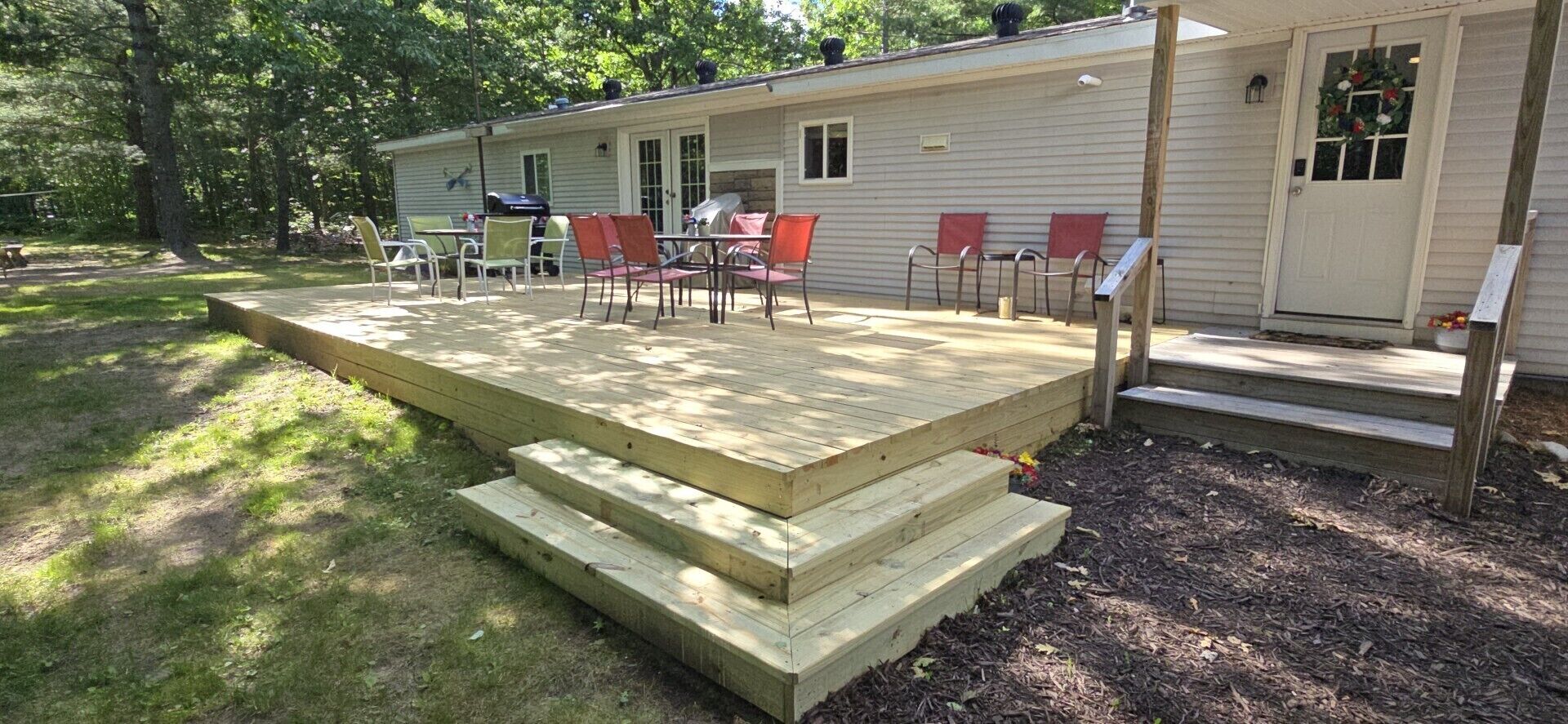 A mobile home with a deck, outdoor seating, and a barbecue grill.