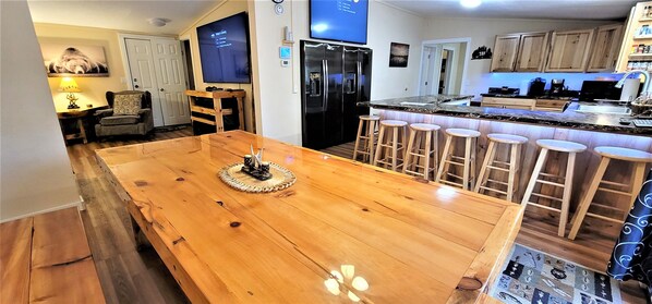 A spacious kitchen with a large wooden island, bar stools, a refrigerator, and a television mounted on the wall.