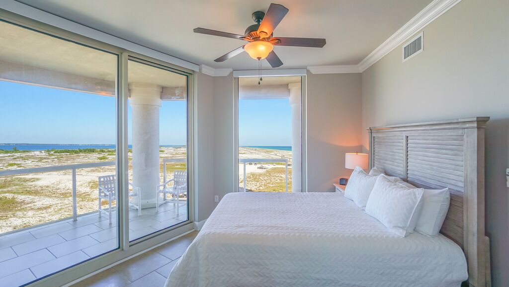 Ein Schlafzimmer mit einem großen Bett, einem Deckenventilator und Blick auf den Strand durch große Schiebeglastüren.