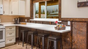 A kitchen with a wooden island, bar stools, and a window overlooking a snowy landscape. - Alaska Back Country Cottages (Palmer)