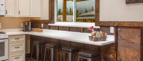 A kitchen with a wooden island, bar stools, and a window overlooking a snowy landscape.