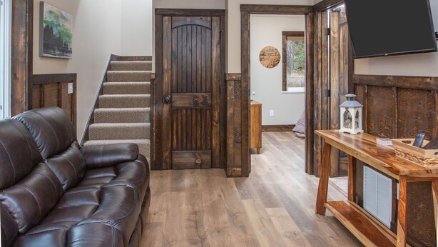 A wooden staircase leading to a second floor, a leather sofa, a wooden table with a lantern, and a television mounted on the wall. - Alaska Back Country Cottages (Palmer)