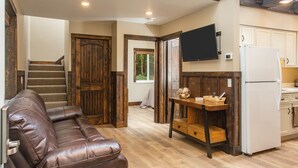 A modern kitchen with wooden flooring, a built-in refrigerator, and a wooden dining table with a basket. - Alaska Back Country Cottages (Palmer)