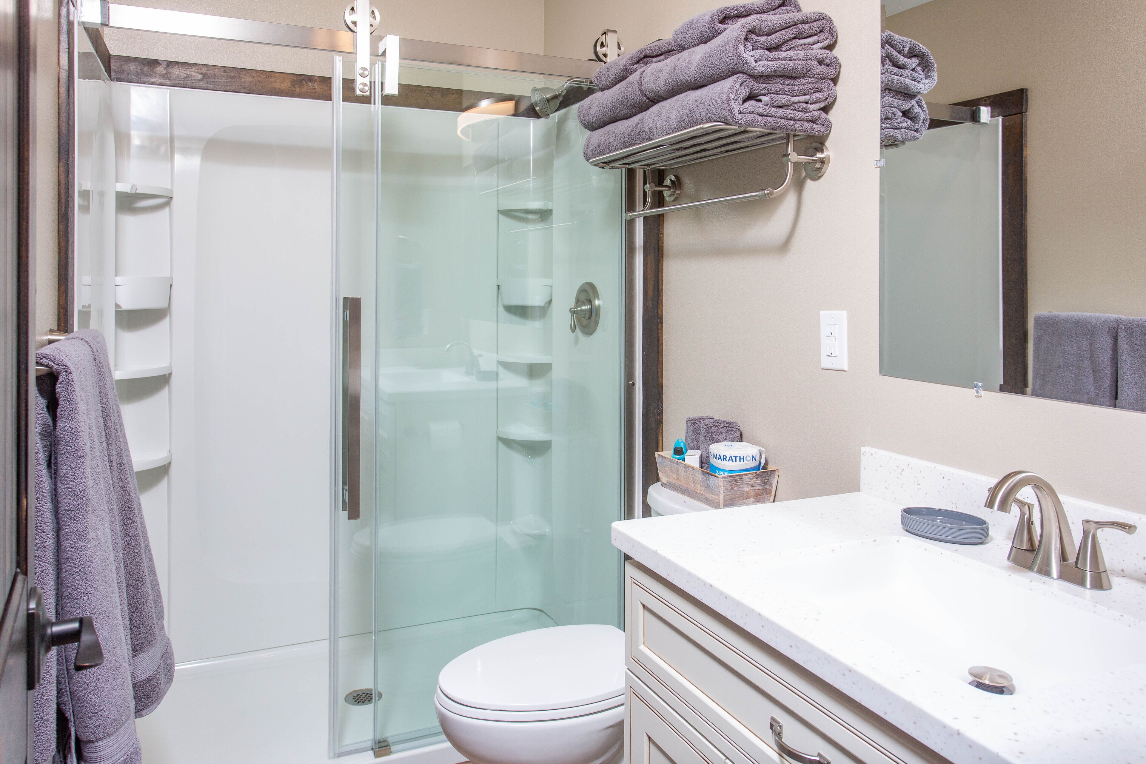 A modern bathroom with a glass-enclosed shower, a white toilet, and a vanity with a sink and mirror.