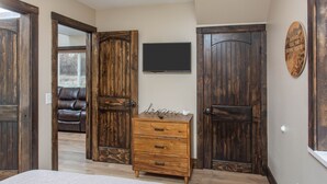 A bedroom with a wooden dresser, a television on the wall, and two large wooden doors. - Alaska Back Country Cottages (Palmer)