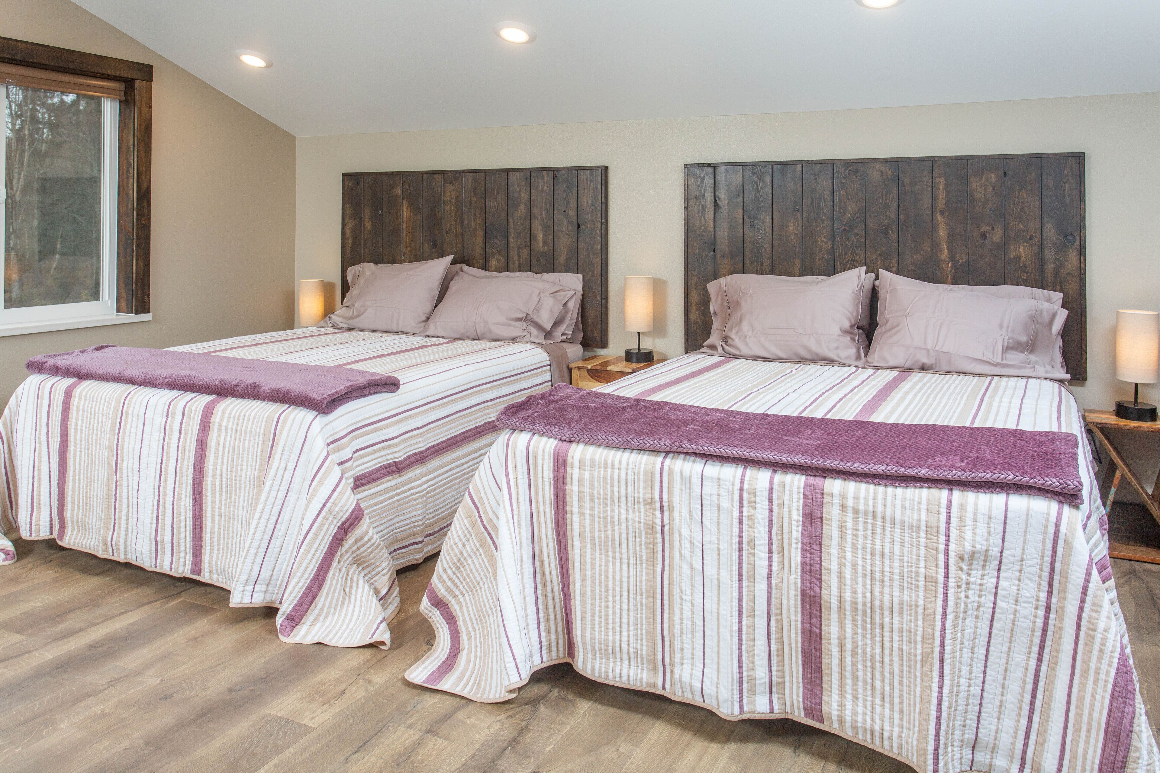 A double room with two beds, each with a wooden headboard, a window, and a nightstand with a lamp.
