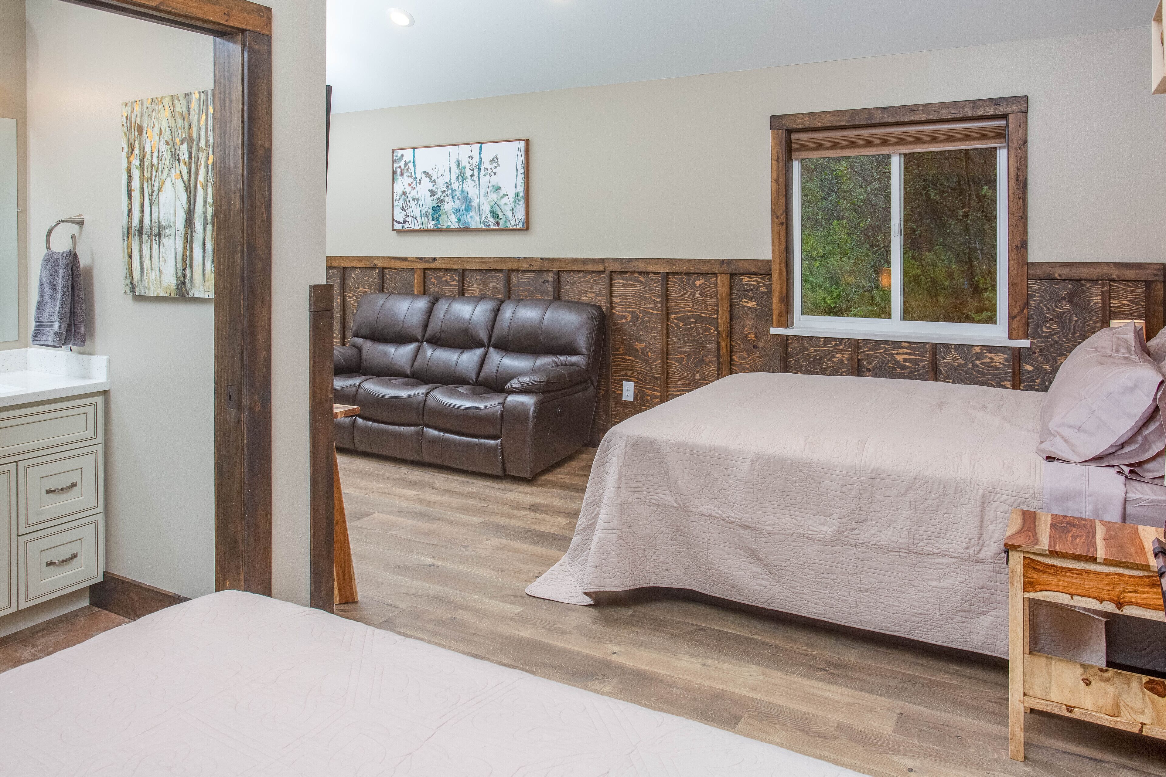 Un dormitorio con una cama, cabecera de madera, ventana con vista a follaje y un sofá de cuero marrón.