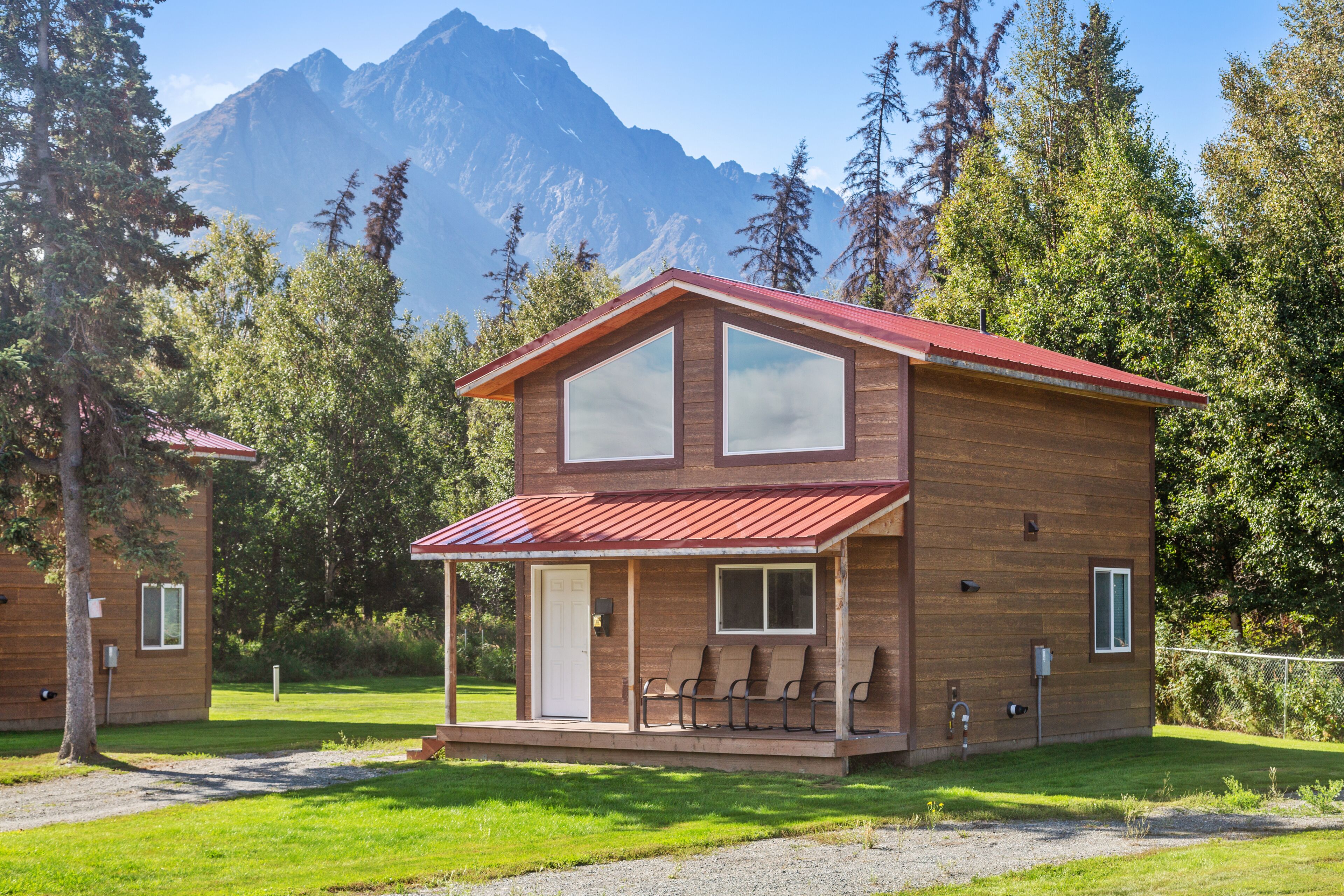 Une cabane en bois à deux étages, avec un toit rouge, de grandes fenêtres et une véranda couverte équipée de chaises.