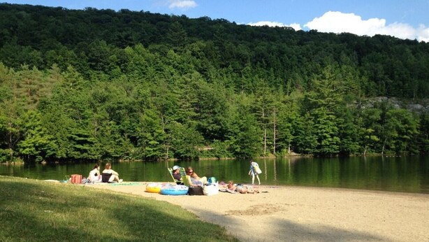 A lakeside setting with people relaxing on the shore, surrounded by dense forest.
