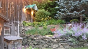 A rustic wooden building with a stone retaining wall and a variety of colorful flowers and plants.
