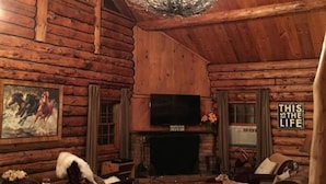 A cozy log cabin interior with a fireplace, a chandelier, a television, and a dog.