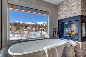 Relax in a serene bathroom with a bathtub and fireplace, offering breathtaking mountain views.