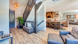 A spacious living area with a staircase, a kitchen with bar stools, and a seating area with a plant. - Creekside Escape: Breck Home, Hot Tub & Steam Shower, Walk to Shuttle! (Breckenridge)