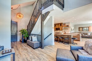 Spacious living area with a kitchen, dining, and seating space, featuring a staircase and a large pendant light.