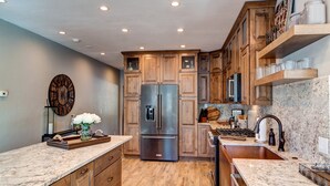 A kitchen with wooden cabinets, a stainless steel refrigerator, granite countertops, and a built-in oven. - Creekside Escape: Breck Home, Hot Tub & Steam Shower, Walk to Shuttle! (Breckenridge)