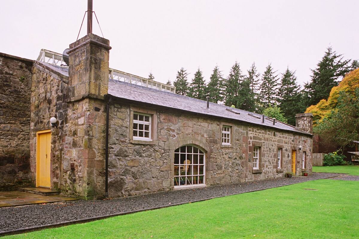 A stone building with a yellow door, a large arched window, and a small window with a white frame.