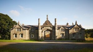 A large stone building with a central archway, multiple chimneys, and a paved driveway. - Blairquhan Cottages (Maybole)