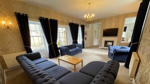 A living room with a large sectional sofa, two armchairs, a coffee table, and a fireplace. - Blairquhan Cottages (Maybole)
