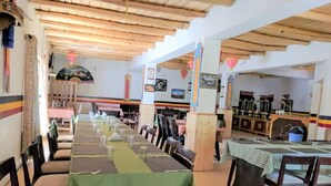 A restaurant with long communal tables, wooden beams on the ceiling, and traditional decor. - Apple Cottage Nubra - Glamping (Leh)