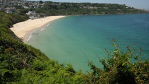 A coastal view with a sandy beach, clear turquoise waters, and a backdrop of residential buildings. - Halwell Lodge (St Ives)