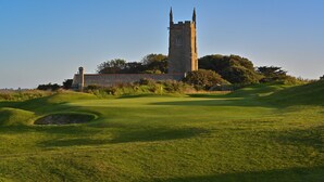 A golf course with a historic tower and a stone building in the background. - Halwell Lodge (St Ives)