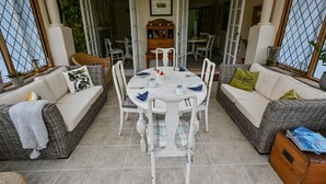 A sunlit patio with wicker furniture, a dining table set for four, and a piano in the background. - Halwell Lodge (St Ives)