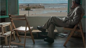A man sitting by a window overlooking a beach with boats and a lighthouse. - Halwell Lodge (St Ives)