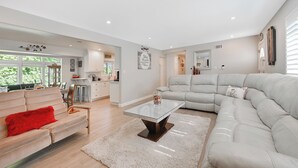 A spacious living area with a large sectional sofa, a glass coffee table, and a red throw pillow.