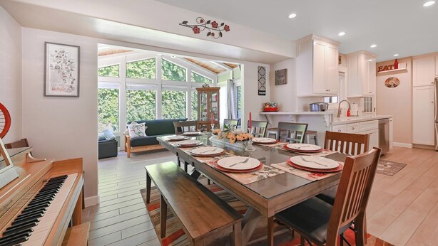 A spacious dining area with a wooden table set for four, a piano, and a view of a green outdoor space.