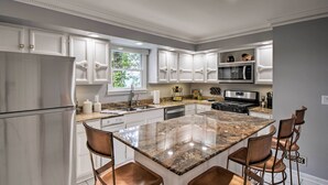 Uma cozinha moderna com armários brancos, bancadas de granito, eletrodomésticos de aço inoxidável e uma ilha central com banquetas.