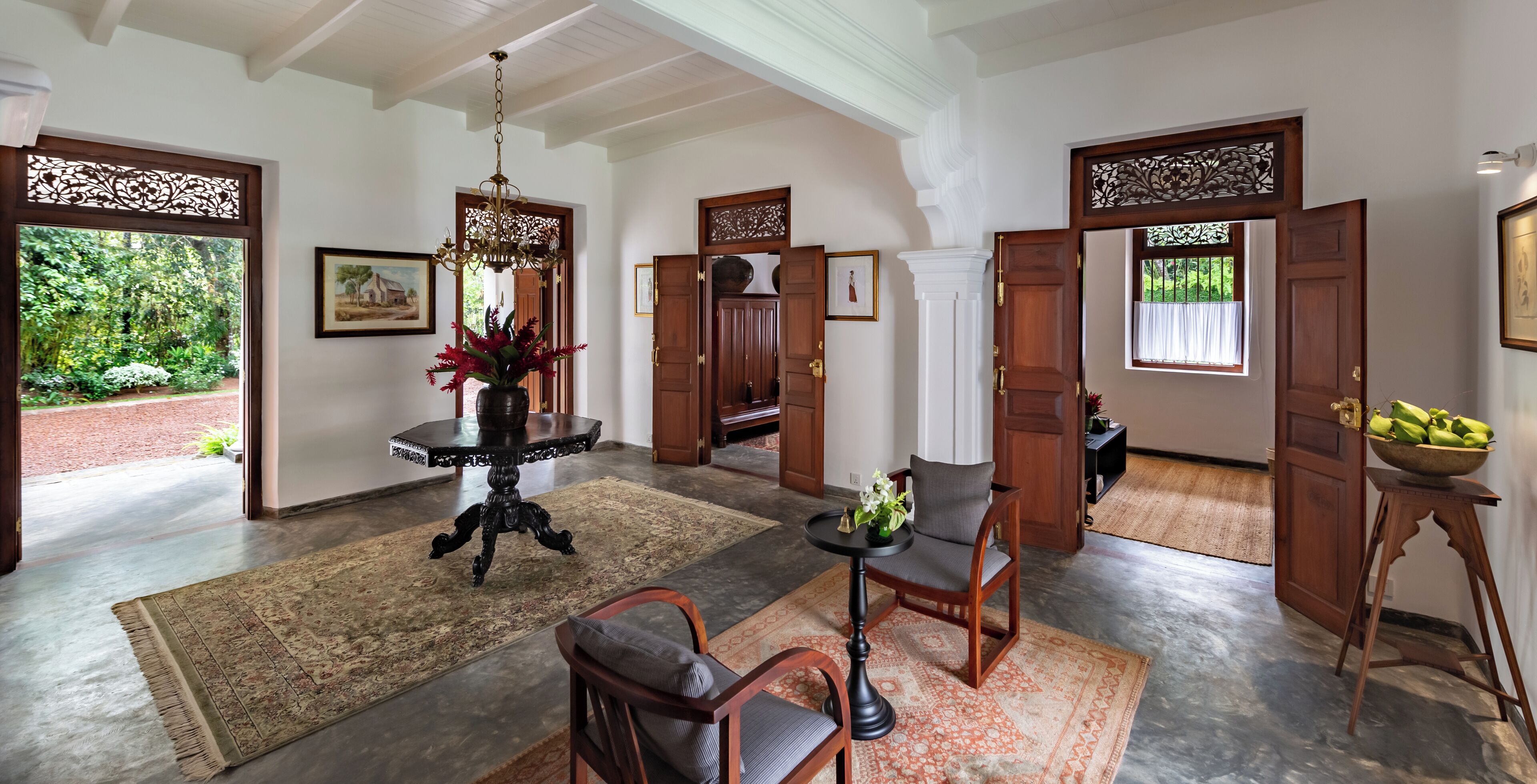 A spacious foyer with a chandelier, wooden doors, and a large rug.