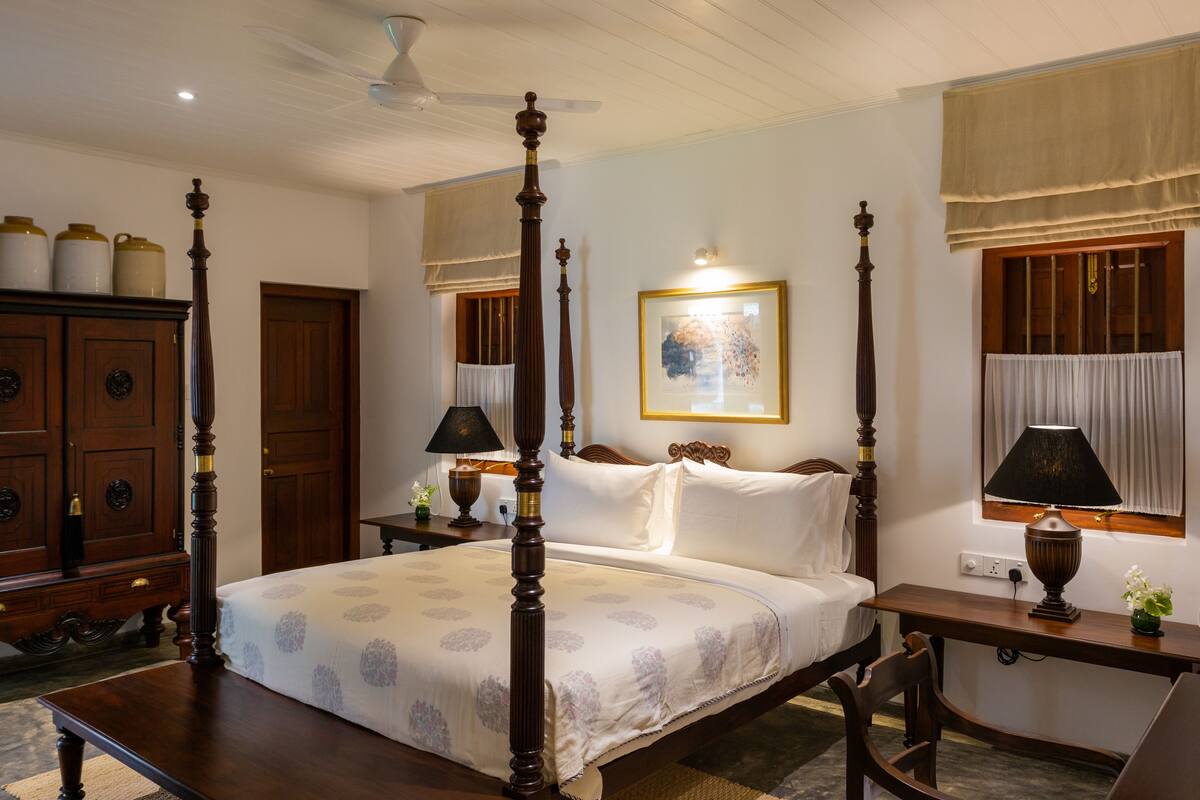 A four-poster bed with a canopy, wooden furniture, and a painting on the wall.