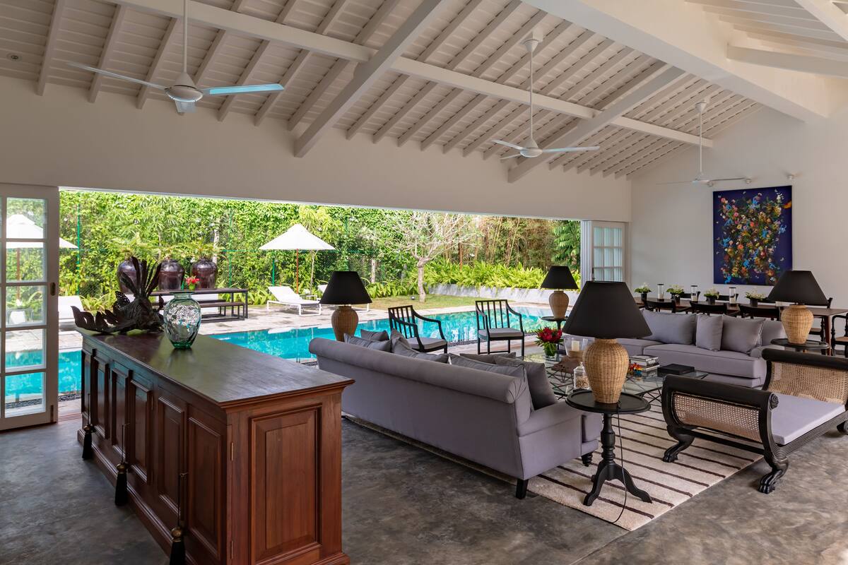 A spacious living area with a pool, outdoor furniture, and a view of lush greenery.
