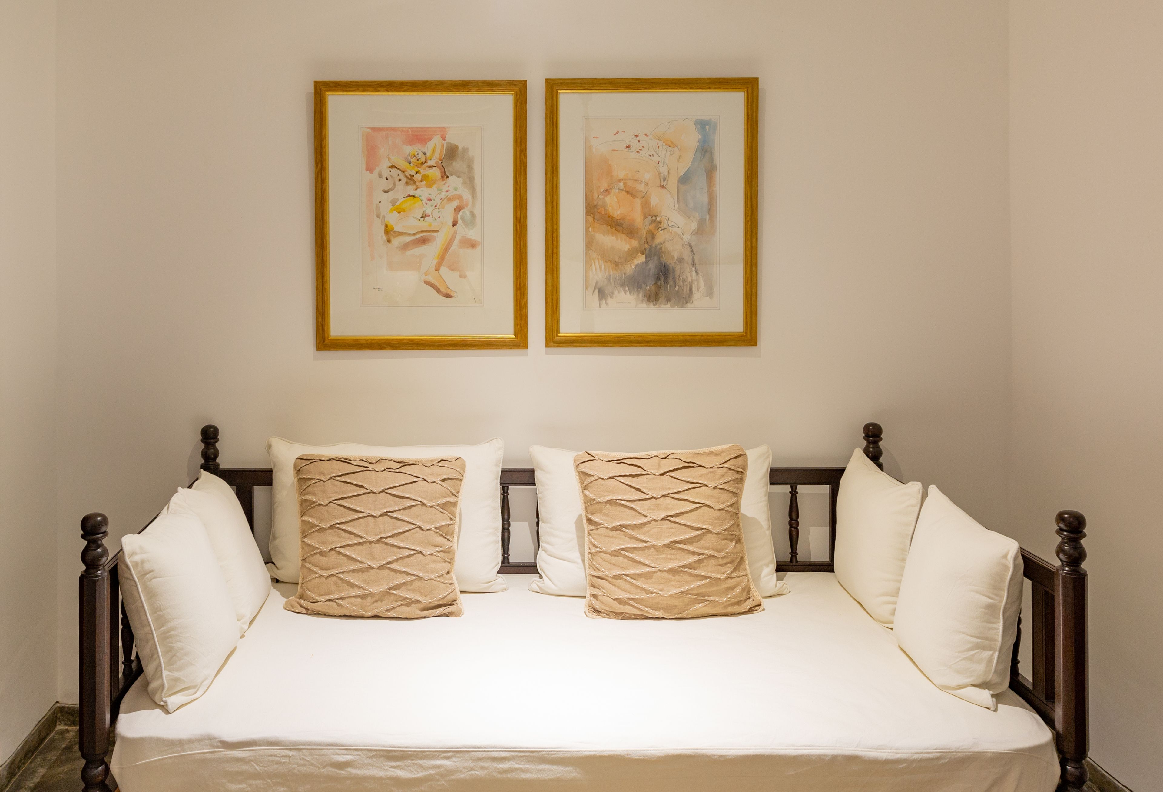 Un lit avec un cadre en bois, une literie blanche et deux coussins décoratifs. Deux œuvres d’art encadrées sont accrochées au mur au-dessus du lit.