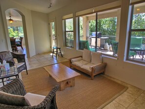 A spacious living area with a large window, a wooden coffee table, wicker furniture, and a view of the outdoors.