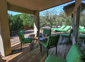 Una terraza de madera con sillas verdes a rayas y una mesa, con vistas a un jardín con árboles y una valla de madera.