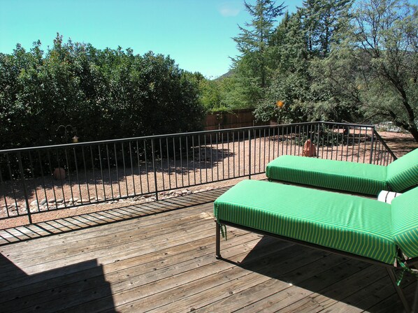 A wooden deck with a metal railing, green striped cushions, and a view of a landscaped garden with trees and shrubs.