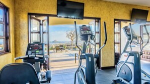 Une salle de sport équipée de machines de cardio, d’un téléviseur et de grandes fenêtres donnant sur l’extérieur.