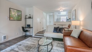 A modern living room with a leather sofa, a glass coffee table, and a white rug. There is a dining area with a table and chairs, and a kitchen in the background. - Moon River Suites 3 - on River, Private Hot Tub, Downtown by North Bend Escapes (North Bend)