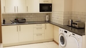 Une cuisine compacte avec des meubles blancs, un four à micro-ondes Bosch, un lave-linge et un grille-pain.