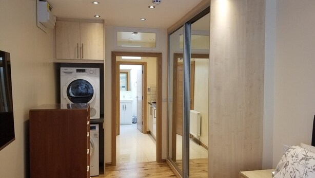 Une chambre moderne comprenant un lit, une armoire en bois, un lave-linge et une porte-fenêtre coulissante donnant sur une salle de bain.