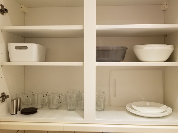 Ett köksskåp med fyra hyllor, där varje hylla innehåller olika typer av köksredskap.