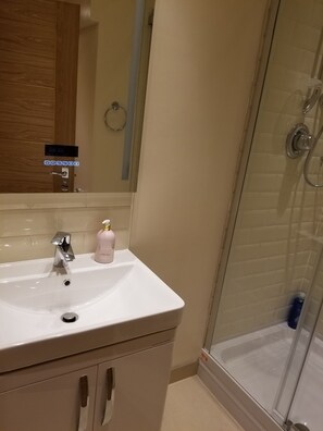 Ein Badezimmer mit einem weißen Waschbecken, einem Spiegel, einer Dusche und einem Holzkabinet.